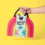 Hand holding a pink arch-shaped Montessori play kit against a yellow background